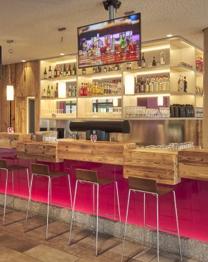 Moderne Hotelbar mit auffälligen roten Barhockern, Holzoberflächen und gut sichtbarem Getränkeangebot.