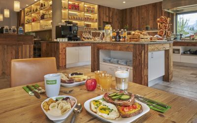 Gedeckter Frühstückstisch vor dem Buffet mit Müsli, frischem Obst, Kaffee und Säften.