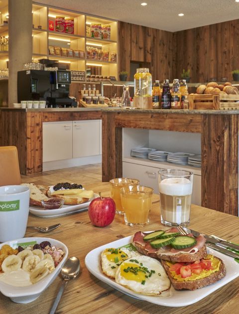 Une table de petit-déjeuner dressée devant le buffet avec du muesli, des fruits frais, du café et des jus de fruits.