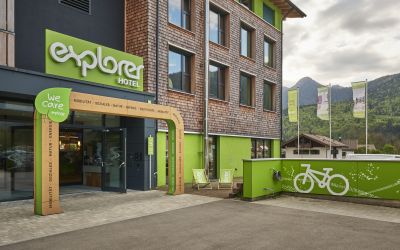 Wejście do hotelu Explorer z rowerami przed budynkiem. Widok zewnętrzny wejścia do hotelu z zieloną, firmową fasadą i zaparkowanymi rowerami.