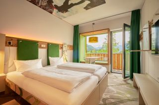 Modernes Doppelzimmer mit Holzelementen, grünen Farbakzenten und direktem Zugang zum Balkon.