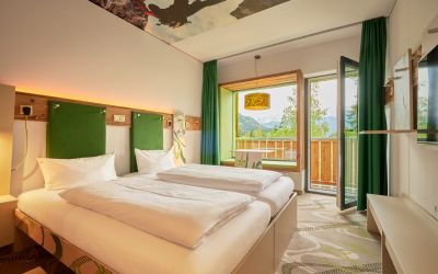 Modernes Doppelzimmer mit Holzelementen, grünen Farbakzenten und direktem Zugang zum Balkon.