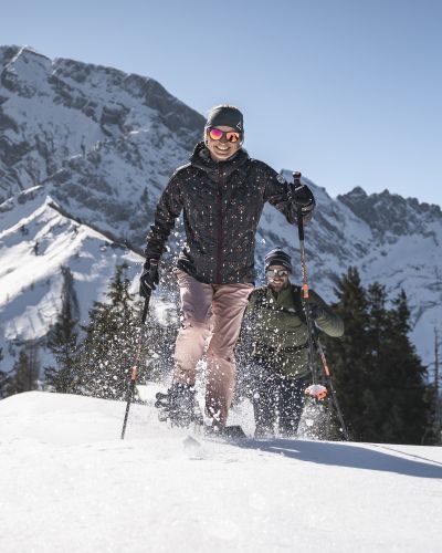 Ein Paar beim Schneeschuhwandern am Rossfeld in Berchtesgaden vor einer traumhaften Bergkulisse im Tiefschnee.
