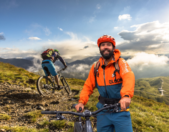 Twee mensen fietsen op mountainbikes in de bergen. Het is zonnig met wolken aan de hemel.