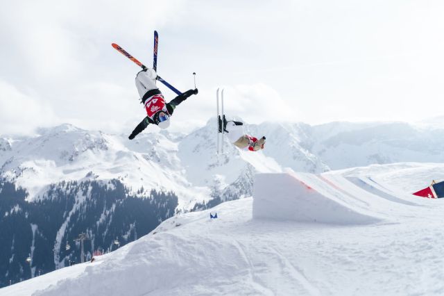 Ein Skifahrer führt einen Trick in den Alpen durch. Es schneit und der Himmel ist bewölkt.