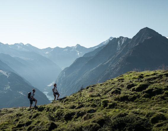 Zwei Wanderer sind am Penken vor einer weiten alpinen Bergkulisse unterwegs