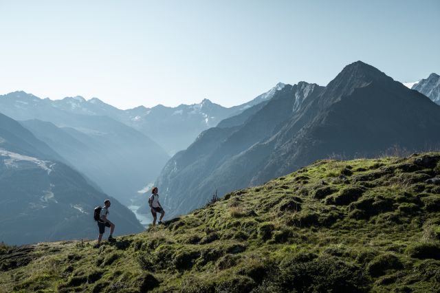 Zwei Wanderer sind am Penken vor einer weiten alpinen Bergkulisse unterwegs