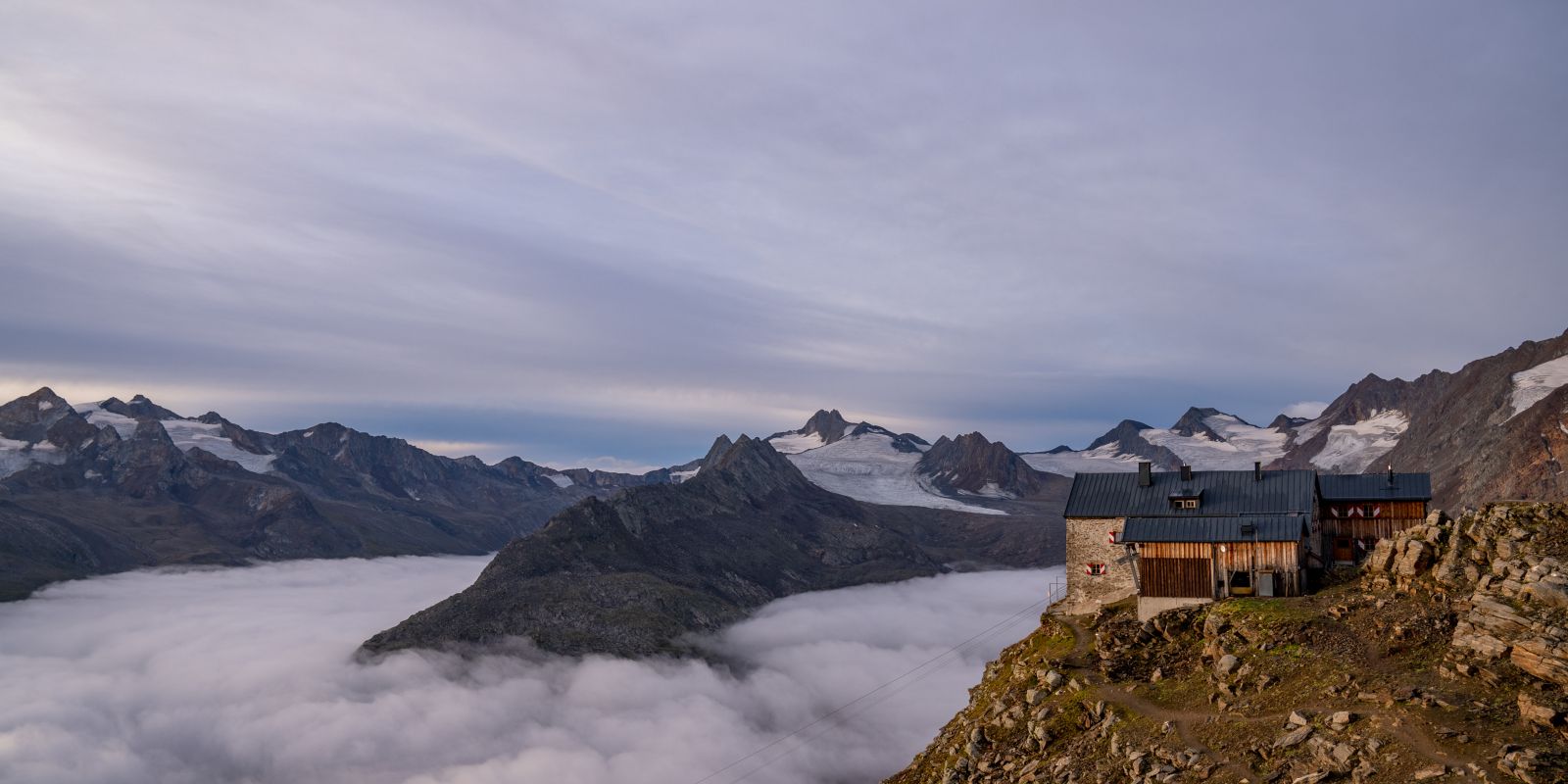 Berghütte auf Felsvorsprung und Gletscherlandschaft.