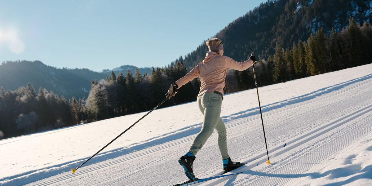 Langläuferin im klassischen Stil auf einer sonnigen Loipe in Bayrischzell Klassischer Langlauf auf einer präparierten Loipe in Bayrischzell mit winterlicher Bergkulisse