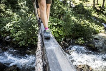 Schritt für Schritt über die Fluss- Brücke in den Bergen