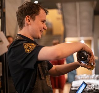Ein Barkeeper steht an der Theke und schüttet ein Getränk aus einer Flasche in ein Glas.