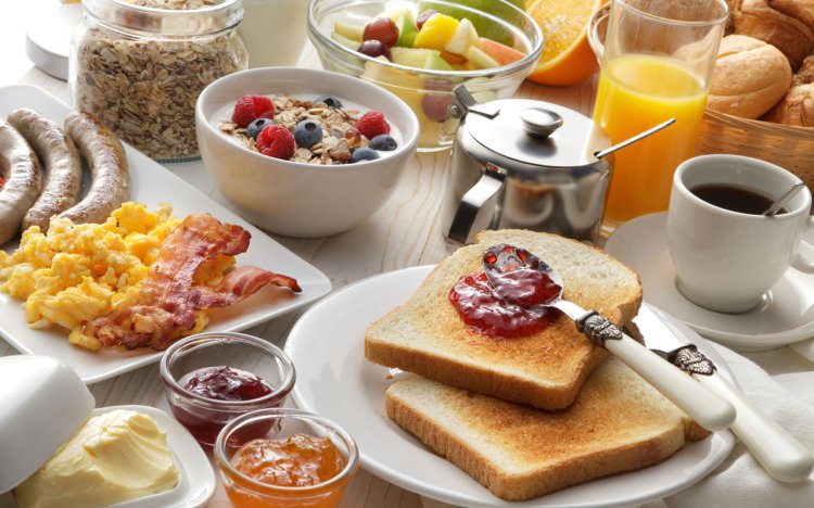 Reichhaltig gedeckter Frühstückstisch mit Toast, O-Saft, Marmelade, Ei und Obst