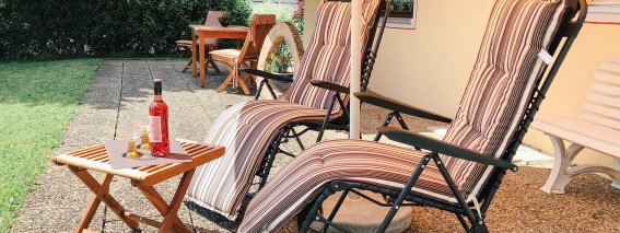 Zwei Liegestühle stehen auf der Terrasse, ein Tisch mit Getränken lädt zum Entspannen ein. Ein schöner Sommertag.