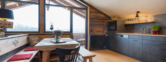 In der Hütte gibt es eine Küche mit Tisch, Stühlen und Fenstern. Es ist Tageslicht zu sehen und die Aussicht ist schön.