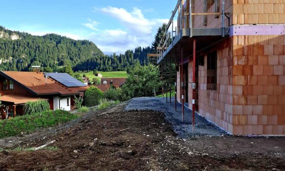 Ein neues Gebäude wird in einer idyllischen Bergregion errichtet, umgeben von Natur und traditionellen Häusern.