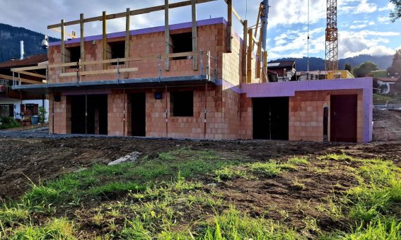 Ein Gebäude in der Bauphase mit sichtbaren Mauern und Holzrahmen in einer ländlichen Umgebung.