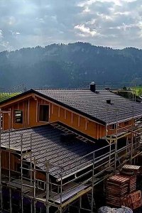 Ein neues Haus wird in einer malerischen Berglandschaft gebaut. Bauarbeiten beginnen bei wechselhaftem Wetter.