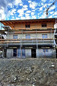 Ein neues Haus wird in den Bergen gebaut. Scaffolding umgibt das Gebäude, während die Arbeiten fortschreiten.
