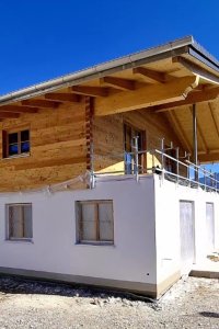 Ein neu gebautes Holzhaus in den Bergen unter klarem Himmel zeigt eine moderne Architektur und natürliche Materialien.