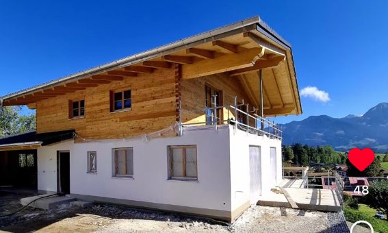 Ein neu gebautes Holzhaus in den Bergen unter klarem Himmel zeigt eine moderne Architektur und natürliche Materialien.