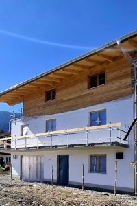 Ein neues Haus wird in den Alpen gebaut, umgeben von Bäumen und Bergen bei klarem, sonnigem Wetter. Buind Hisle, Obermaiselstein