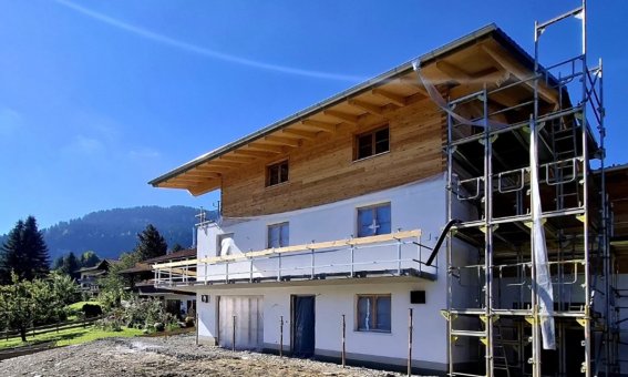 Ein neues Haus wird in den Alpen gebaut, umgeben von Bäumen und Bergen bei klarem, sonnigem Wetter. Buind Hisle, Obermaiselstein