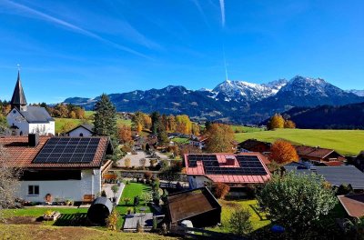 Ein malerisches Dorf am Fuß der Berge, umgeben von buntem Herbstlaub und strahlend blauem Himmel.