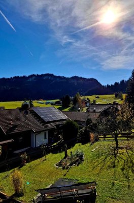 Sonnenstrahlen scheinen über grüne Wiesen und Hütten in einem ruhigen bayerischen Dorf im Herbst.