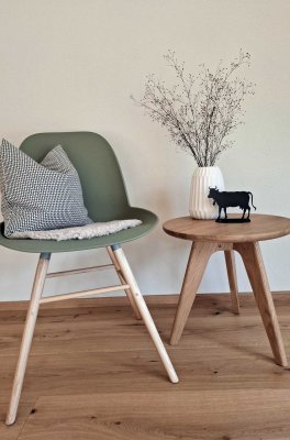 Ein Stuhl steht neben einem Tisch mit einer Vase und einer kleinen Figur. Auf dem Tisch liegt ein kleiner Stoff.