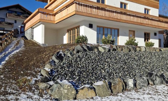 Ein modernes Haus steht in den Bergen. Der Schnee liegt auf dem Boden. Der Himmel ist blau und klar.
