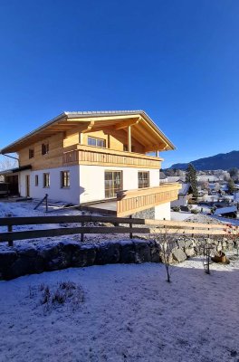 Ein neues Haus steht in einer verschneiten Umgebung. Der Himmel ist blau und die Sonne scheint.