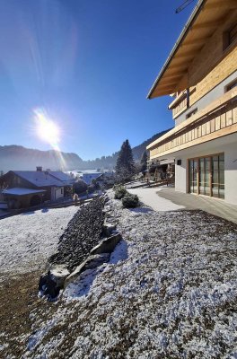 Der Schnee liegt auf dem Boden. Die Sonne scheint. Ein Haus steht in der Landschaft. Bäume sind im Hintergrund sichtbar.