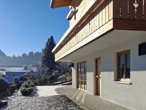 Ein Haus in den Bergen steht im Schnee. Der Himmel ist blau und die Sonne scheint. Es ist Winter.