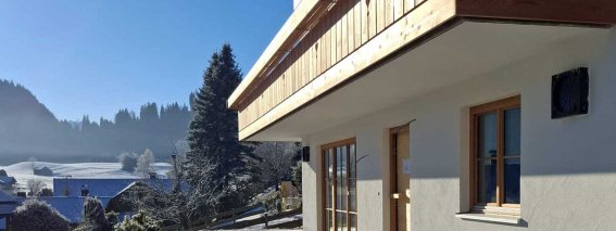 Ein Haus in den Bergen steht im Schnee. Der Himmel ist blau und die Sonne scheint. Es ist Winter.