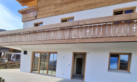 Das Haus hat mehrere Stockwerke und einen großen Balkon. Der Garten ist noch unvollständig und der Boden ist braun.