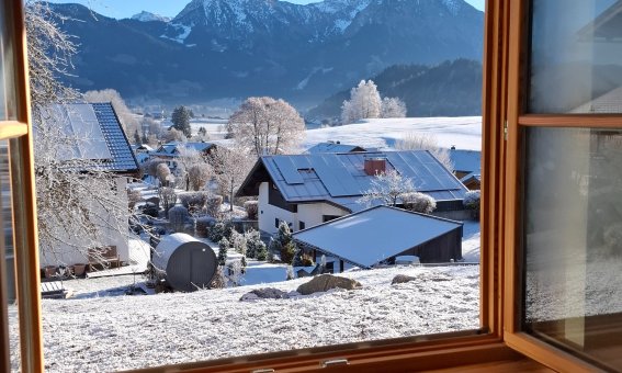 Durch ein offenes Fenster sieht man die verschneite Landschaft und die Berge im Hintergrund an einem klaren Wintertag.
