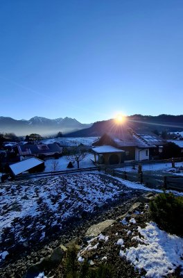 Der Sonnenaufgang beleuchtet ein kleines Dorf in den Bergen. Schnee liegt auf den Dächern und dem Boden.