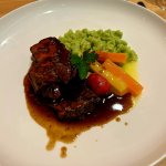 Auf dem Teller liegt Fleisch mit einem Blick auf Gemüse und Püree. Es gibt Tomaten und verschiedene Karottenstücke.