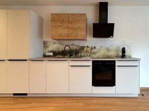 Eine Küche mit weißen Schränken, Holzoberflächen und modernen Geräten. Im Hintergrund sind Landschaftsmotive zu sehen.