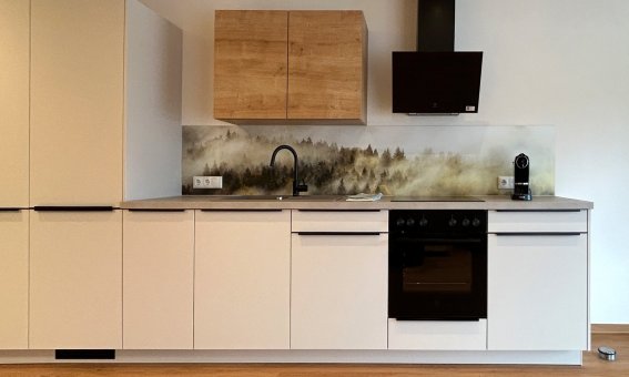 Eine Küche mit weißen Schränken, Holzoberflächen und modernen Geräten. Im Hintergrund sind Landschaftsmotive zu sehen.