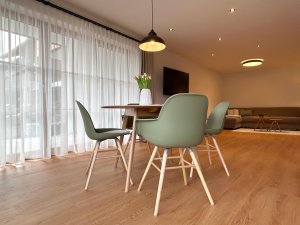 Ein Essplatz mit einem Tisch und Stühlen in einem hellen Raum. Das Licht fällt durch große Fenster und bietet einen offenen Blick.