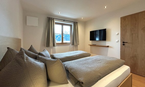 Das Zimmer zeigt zwei Einzelbetten, einen Fernseher und einen Blick auf die Berge. Tageslicht strömt durch das Fenster.