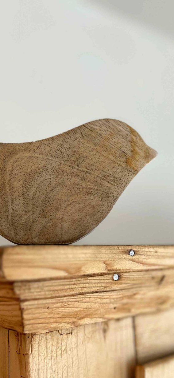 Ein Holzvogel steht auf einem Holzregal. Das Regal ist in einem Raum mit natürlichem Licht.