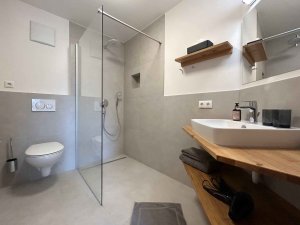 Das Badezimmer zeigt eine Dusche, ein Waschbecken und eine Toilette. Es ist hell und gut organisiert.