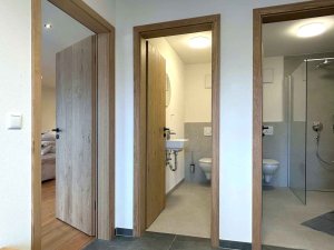 Der Blick zeigt drei Türen in einem Wohnbereich mit einem Bad und einem weiteren Raum im Hintergrund.