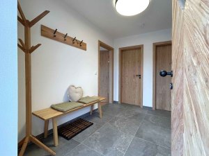 In einem Flur stehen eine Bank und eine Garderobe. Es gibt Türen zu zwei Räumen. Der Boden ist gefliest und hell.