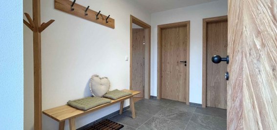 Flur mit Garderobe und Bank in einem Haus In einem Flur stehen eine Bank und eine Garderobe. Es gibt Türen zu zwei Räumen. Der Boden ist gefliest und hell.