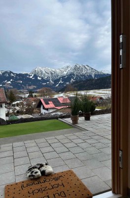 Aus der Tür ist die schneebedeckte Berglandschaft sichtbar. Einige Häuser stehen in der Nähe.