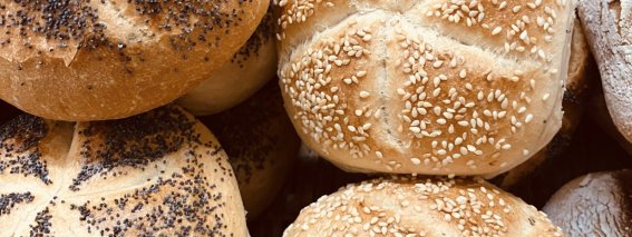 Bunte Brötchen liegen in einem Korb auf einem Markt. Einige sind mit Mohn und andere mit Sesam bestreut.
