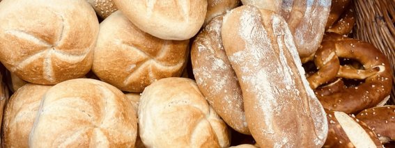 Ein Korb mit verschiedenen Brötchen und Brezeln liegt auf einem Tisch. Die Backwaren sind frisch und gut sortiert.